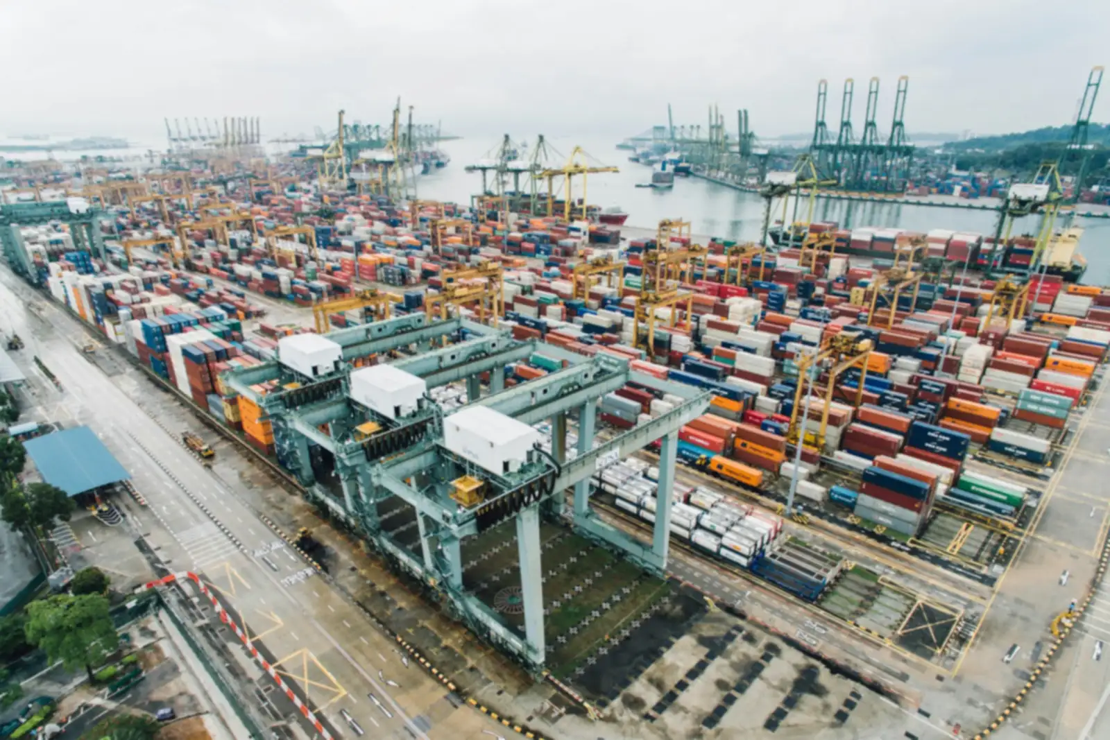 Aerial view of a busy container port with stacked containers, gantry cranes and ships